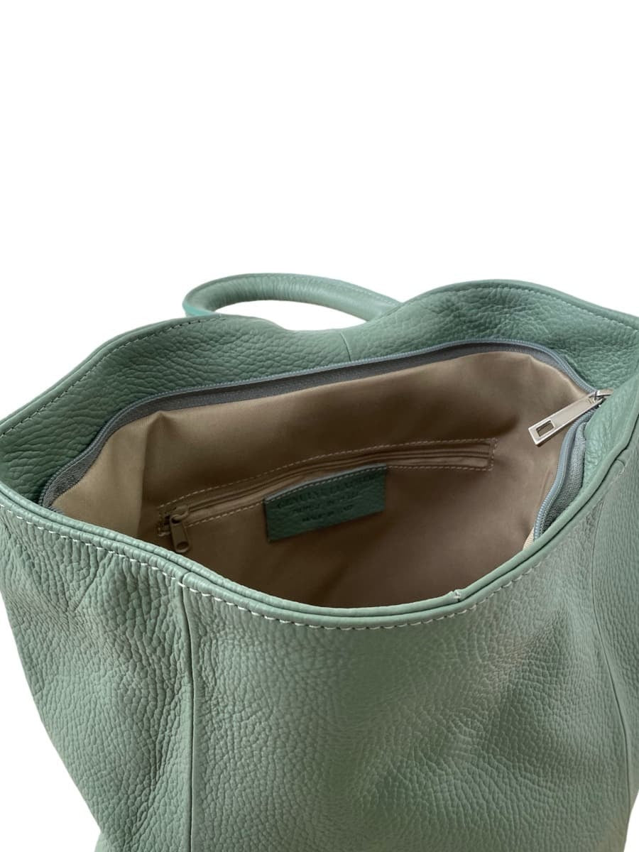 Interior de mochila de cuero verde menta para mujer, con forro beige y bolsillos organizadores con cierre. Espaciosa y elegante, ideal para llevar lo esencial con estilo.